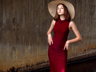 Young girl in luxurious red dress and large hat in a vogue style look posing standing in water...