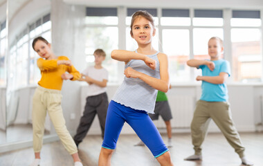 Positive juvenile girl engaged in breakdancing together with children's group in training room during workout session