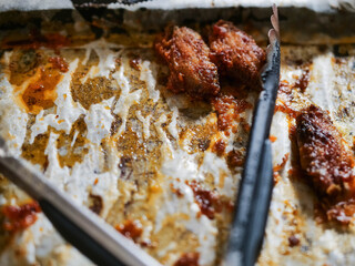 Cooking tray with paper and a few cooked chicken wings and bones and black old tongs. Paper is full of grease.
