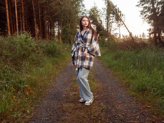 A woman is standing on a dirt road wearing a vogue style jacket and blue jeans. She is looking at...