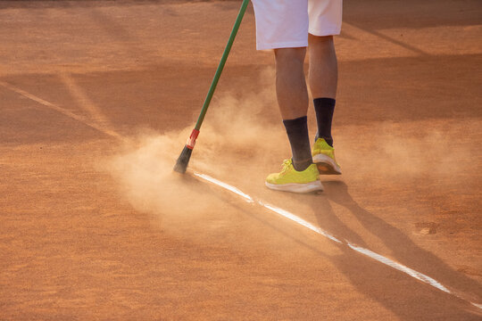 uomo che pulisce le righe del campo da tennis con scopa
