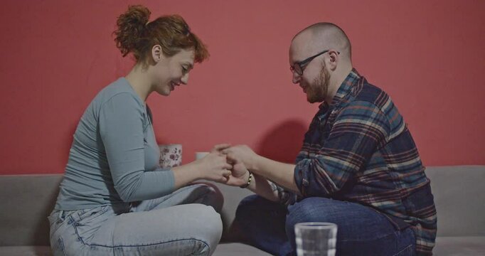 A happy couple spends quality time together on the sofa, playing a hand-clapping game and laughing.