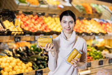 Young woman buyer choosing packaged corn in vegetable shop