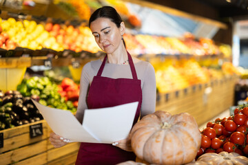 Attentive middle-aged female seller restocking with paper in fruit and vegetable market