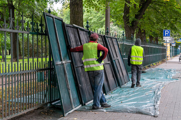 Two municipal workers in high-visibility vests are seen installing or repairing sections of a metal...
