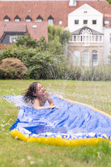 Child enjoying summer water activities on inflatable slide, splashing water in a sunny garden,...