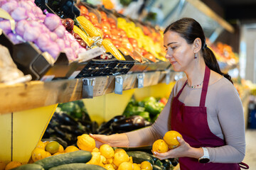 Careful middle-aged saleswoman placing lemons on counter in large grocery store