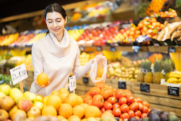 Armenian woman putting ripe oranges in a plastic bag by weighing in the vegetable department of a...