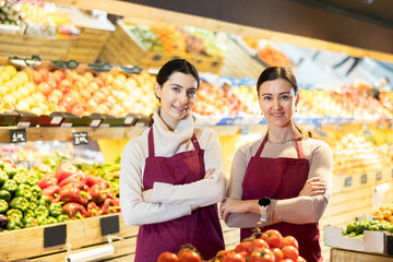 Qualified saleswomen in the vegetable department of the supermarket invite you to buy seasonal vegetables and fruits. Joyful supermarket workers posing at the counter