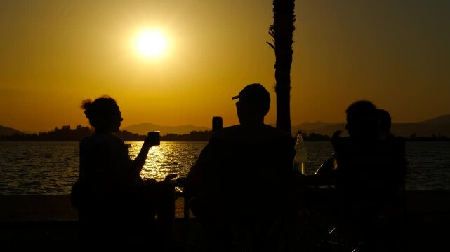 Parents and children will enjoy a bakery at sunset. Silhouettes of a family enjoying a picnic by the sea create a heartwarming scene as the sun sets