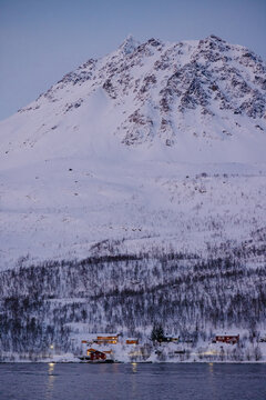 Snow-covered village beneath rugged mountain at dusk