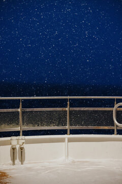 Snowfall on boat deck at night over dark sea