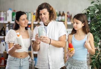 Positive parents and daughter choosing sunscreen in store during summer