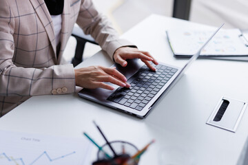 Anonymous woman in checkered jacket typing text on laptop in office
