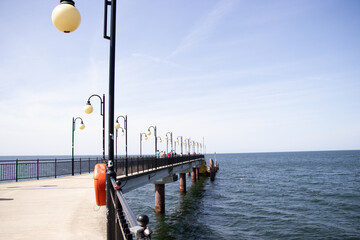 Metal pier with red railings and a lamppost leading to the Baltic Sea on a sunny day. Calm blue...