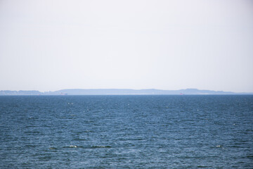 Clear blue horizon separates the light sky and calm water. Minimalist seascape with gentle colors...