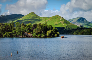 A serene morning view of Derwentwater Lake with Derwent Isle and Catbells fell in the frame, as a ferry boat crosses the water, bathed in soft summer sidelights 1