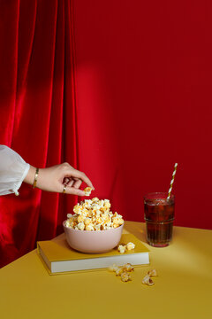 Hand Reaching for Popcorn in Pink Bowl on Yellow Table
