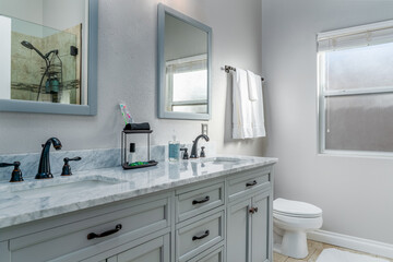 Gray bathroom with double sink marble vanity mirrors, cabinet, towels, and toilet