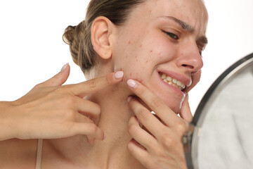 Studio shot of young woman squeezing acne in pain in front of mirror on white background.