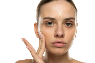 Young woman applying foundation with fingers, studio shot on white background