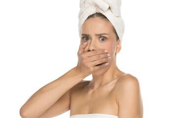 Studio shot on white background of young woman with towel on head covering mouth in shock