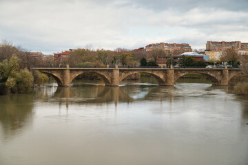 Obraz premium The Logroño Stone Bridge on the Ebro River as it passes through the capital of the autonomous community of La Rioja. With its reflection of the bridge and its clouds