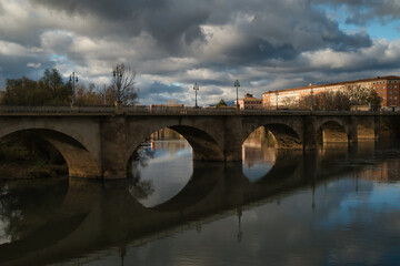 Fototapeta premium The Logroño Stone Bridge on the Ebro River as it passes through the capital of the autonomous community of La Rioja. With its reflection of the bridge and its clouds