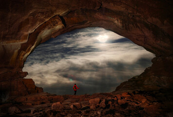 Man tourist in a natural sandstone arch against full moon sky. Window Arch. Utah. Moab. USA