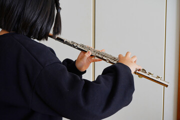室内でフルートを演奏する黒髪の小学生の女の子の横顔