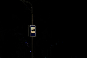 bus stop sign glowing under streetlights during nighttime in a city environment. Captures the quiet...