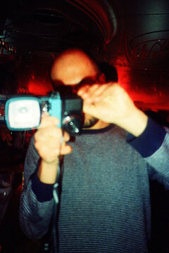 Anonymous Person with Vintage Camera in Dimly Lit red Bar