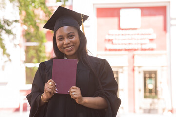 Happy young african woman in graduation gown holding diploma. 