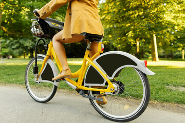 Naklejka premium Woman riding yellow electric bicycle on the park road, cropped closeup shot on female legs and wheels
