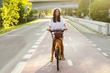 Young happy lady riding electric bicycle on bike path in the park, enjoying sunny day and...