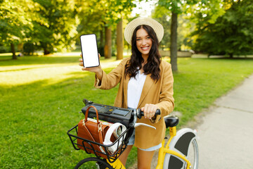 Happy woman renting electric bicycle and showing smartphone with blank screen, mockup. Concept of...