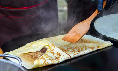 Delicious crepes being expertly folded and cooked on a heated griddle by a chef. The warm steam and...