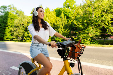 Stylish lady in headphones riding electric bicycle in an urban park setting, enjoying music and...