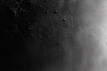 Fototapeta premium Close-up of a textured black surface with uneven rough patches and a gradual light gradient from left to right, creating a moody and abstract atmosphere