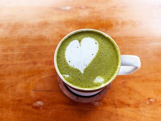 Close-up of a matcha green tea latte with heart-shaped foam art on a wooden table. A cozy and...