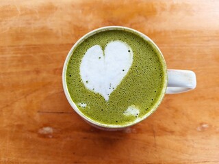 Close-up of a matcha green tea latte with heart-shaped foam art on a wooden table. A cozy and...