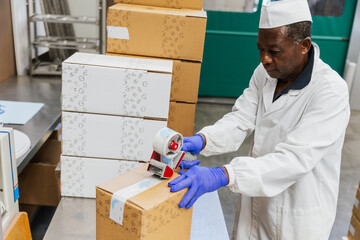 Warehouse worker sealing a cardboard box with tape during packaging process