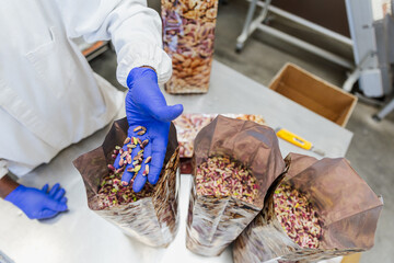 Top view of worker’s hand placing pistachios into a bag during food packaging