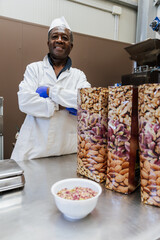Happy warehouse worker with crossed arms standing behind packed pistachios