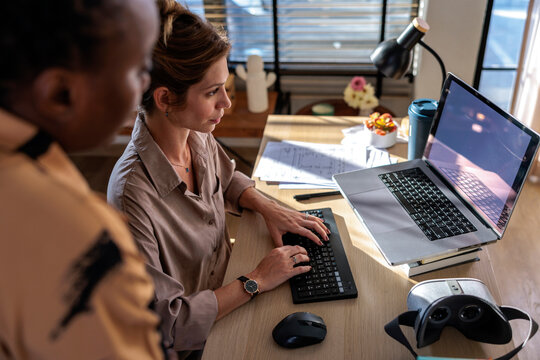 Women Collaborating on Laptop with VR Headset on desk in Office