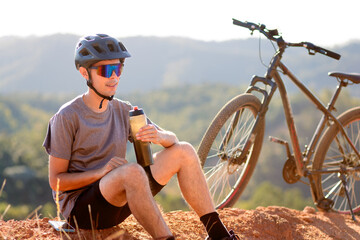 Man resting with a bottle of water next to his bike. Healthy habits, fitness, and connection with...