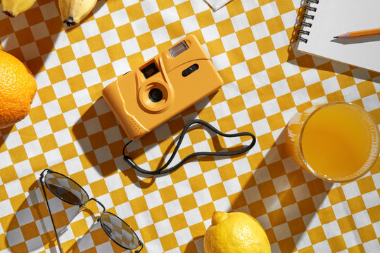 Orange film camera on yellow and white checkered tablecloth.