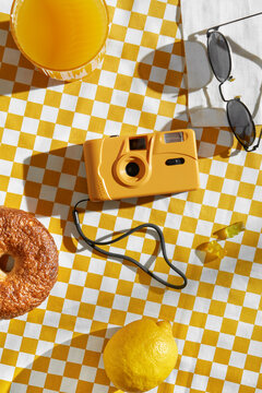 Orange film camera on yellow and white checkered tablecloth.
