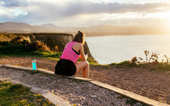 Woman resting by the sea with smartphone at sunset