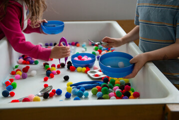 Two preschool kids play with puff balls at a sensory table